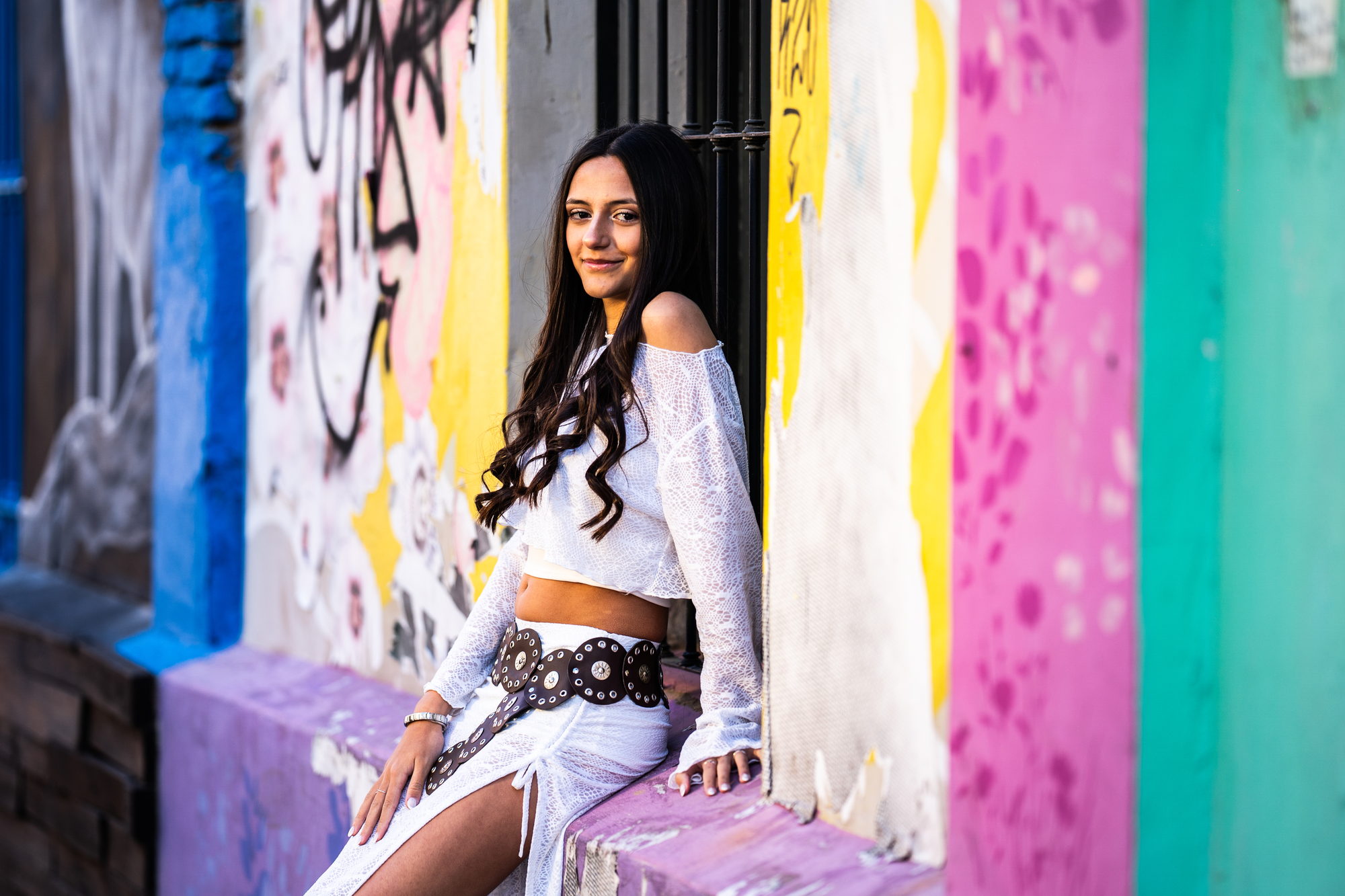 Quinceañera sentada frente a una pared rosa y turquesa