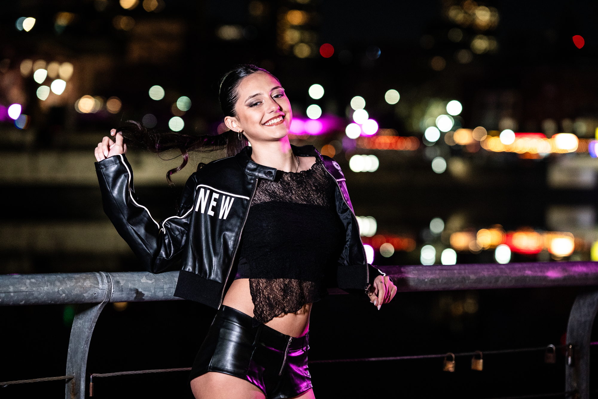 Quinceañera apoyada en una baranda con la ciudad iluminada detrás