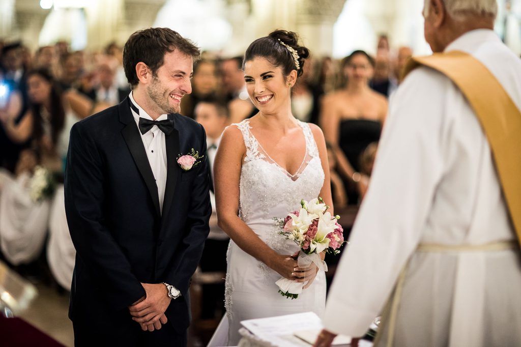 Novios riéndose durante la ceremonia religiosa mientras el sacerdote les habla, casamiento en Buenos Aires
